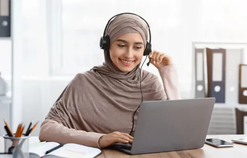 Eine Frau sitzt vor ihrem PC zuhause und lacht weil sie dank new work flexibel arbeiten kann